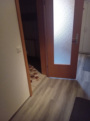 A hallway with a wooden door, a tiled floor, and a carpeted area.