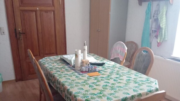 Un coin repas avec une table dressée pour quatre personnes, des chaises en bois, un buffet et une fenêtre avec des rideaux.