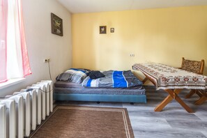 A compact room with a bed, a table, a chair, a radiator, and a window with curtains. - Apartment 'Familienzimmer Am See' with Shared Terrace, Shared Garden and Wi-Fi (Schkeuditz)