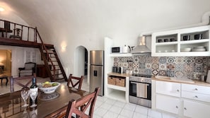 A modern kitchen with a stainless steel refrigerator, microwave, and oven, a wooden dining table with chairs, and a staircase leading to an upper level. - Villa LuxL Manor House (Mesaria)