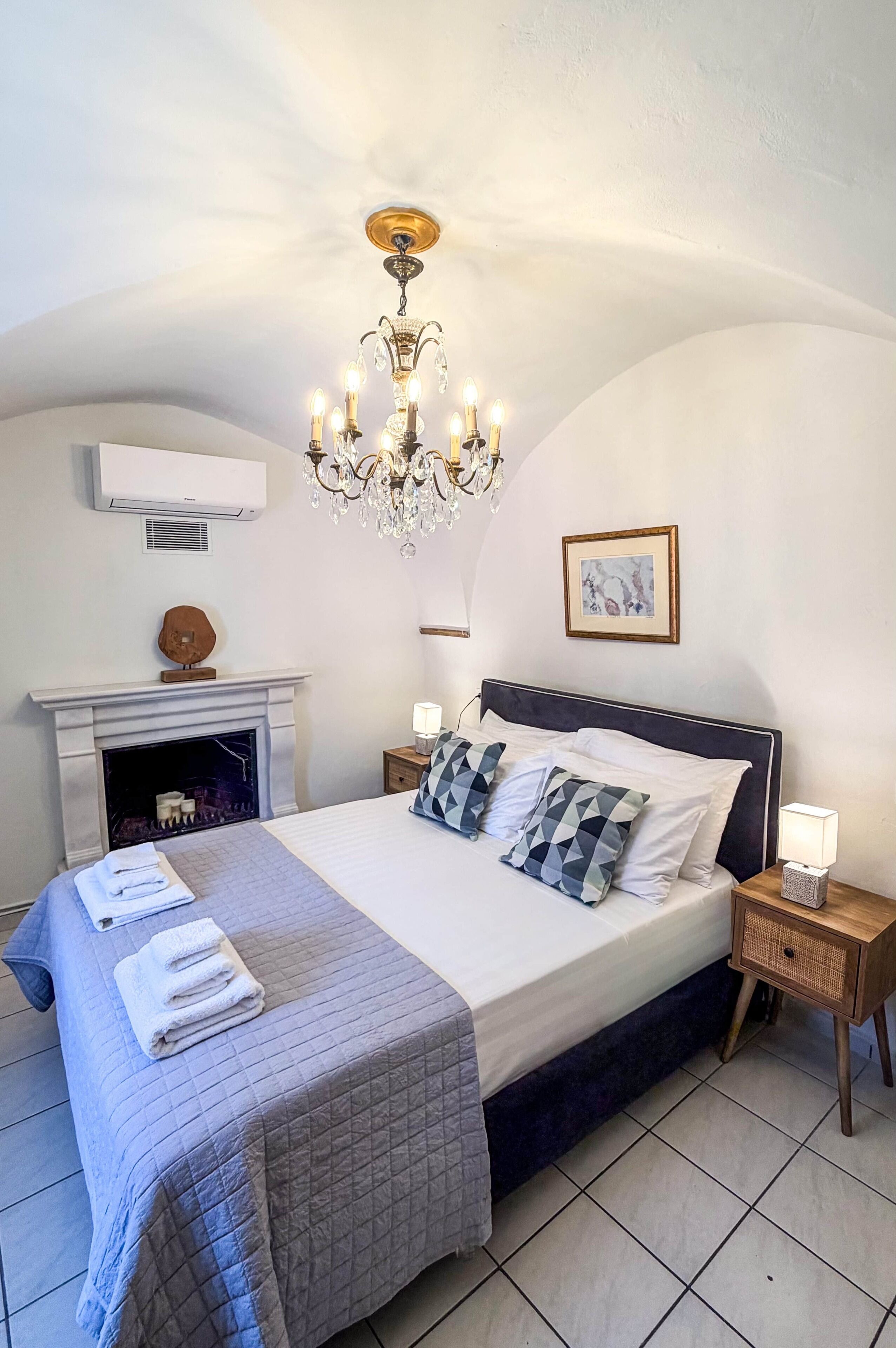 Een slaapkamer met een groot bed, een kroonluchter, een open haard en een ingelijst schilderij aan de muur.