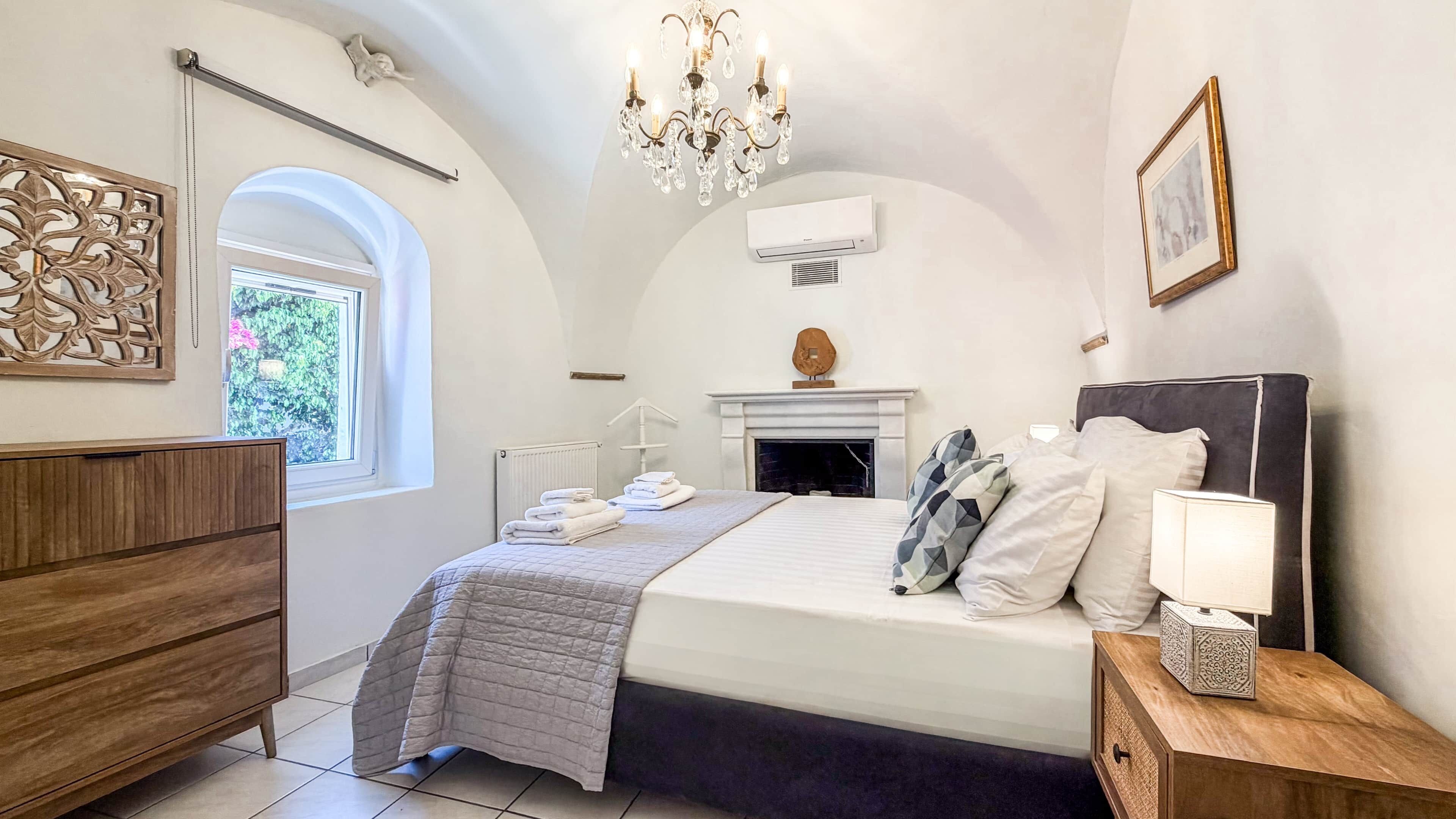 Un dormitorio con cama, cómoda, candelabro, chimenea y ventana.
