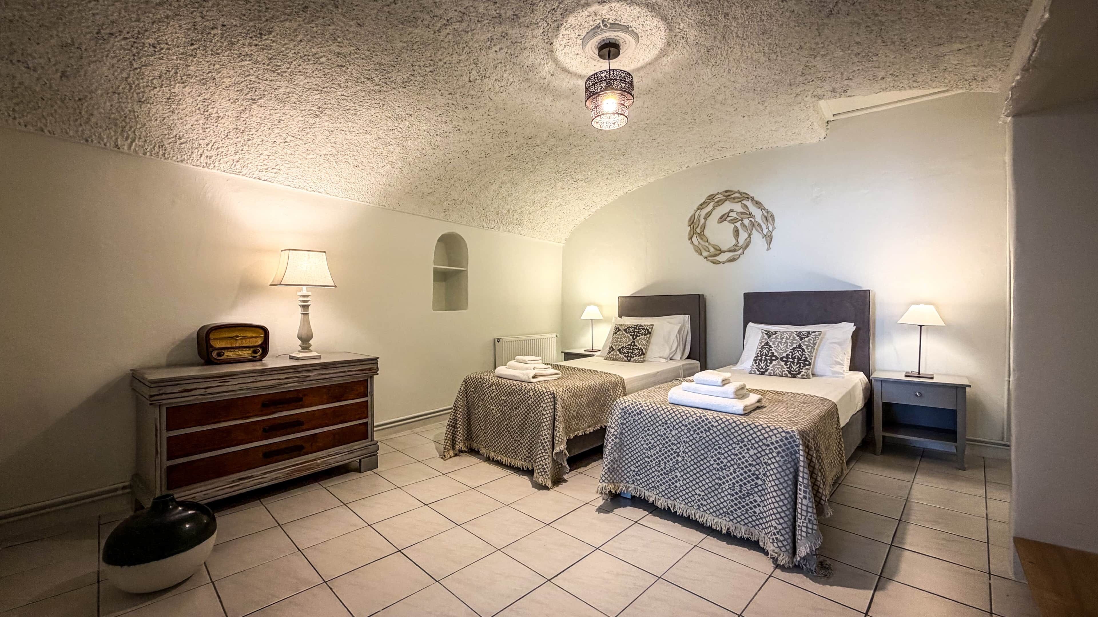Une chambre avec deux lits, une commode, une lampe et un luminaire décoratif au plafond.