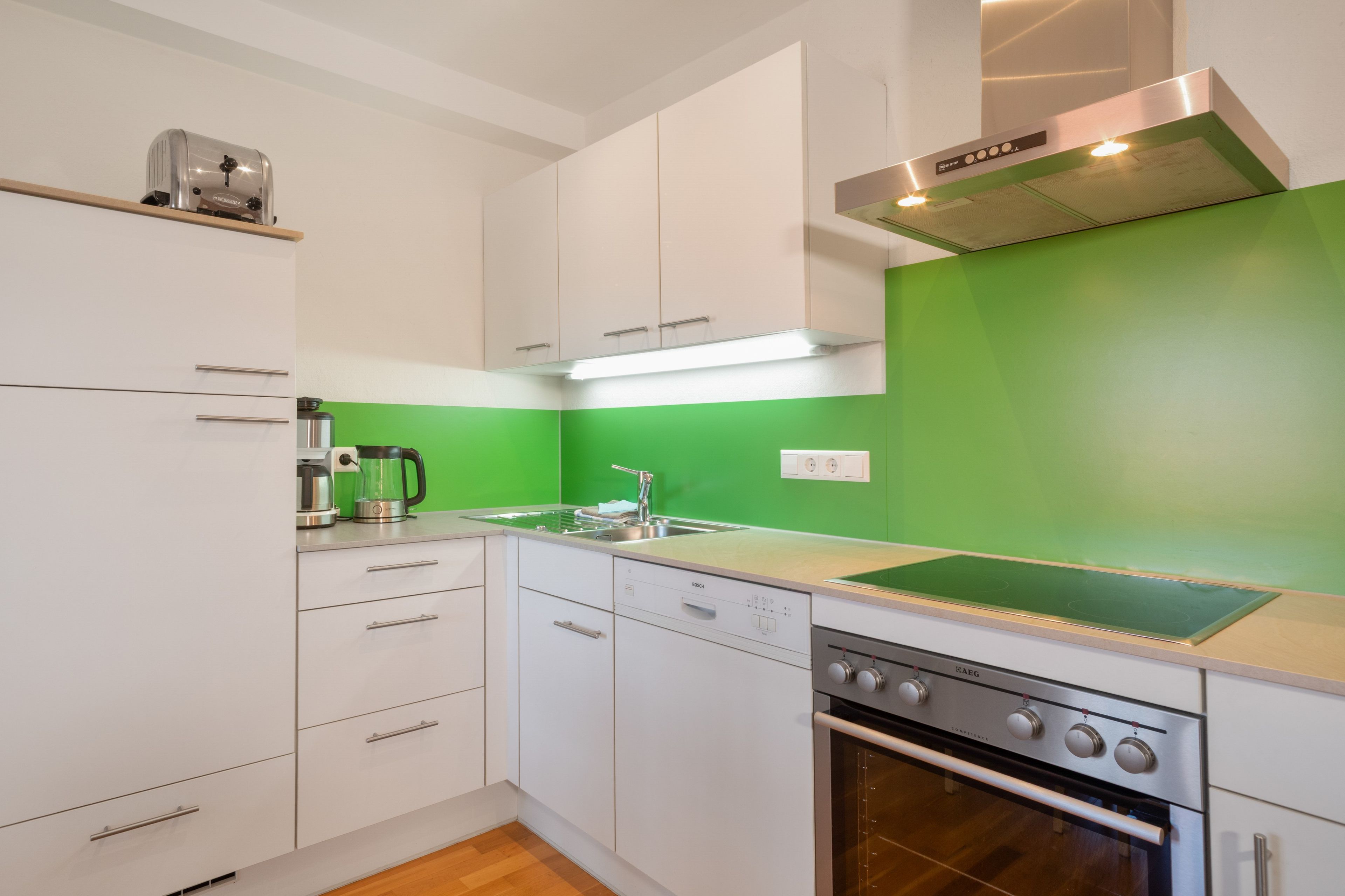 Een moderne keuken met witte kasten, een vaatwasser van Bosch, een oven van Bosch en een groene spatwand.
