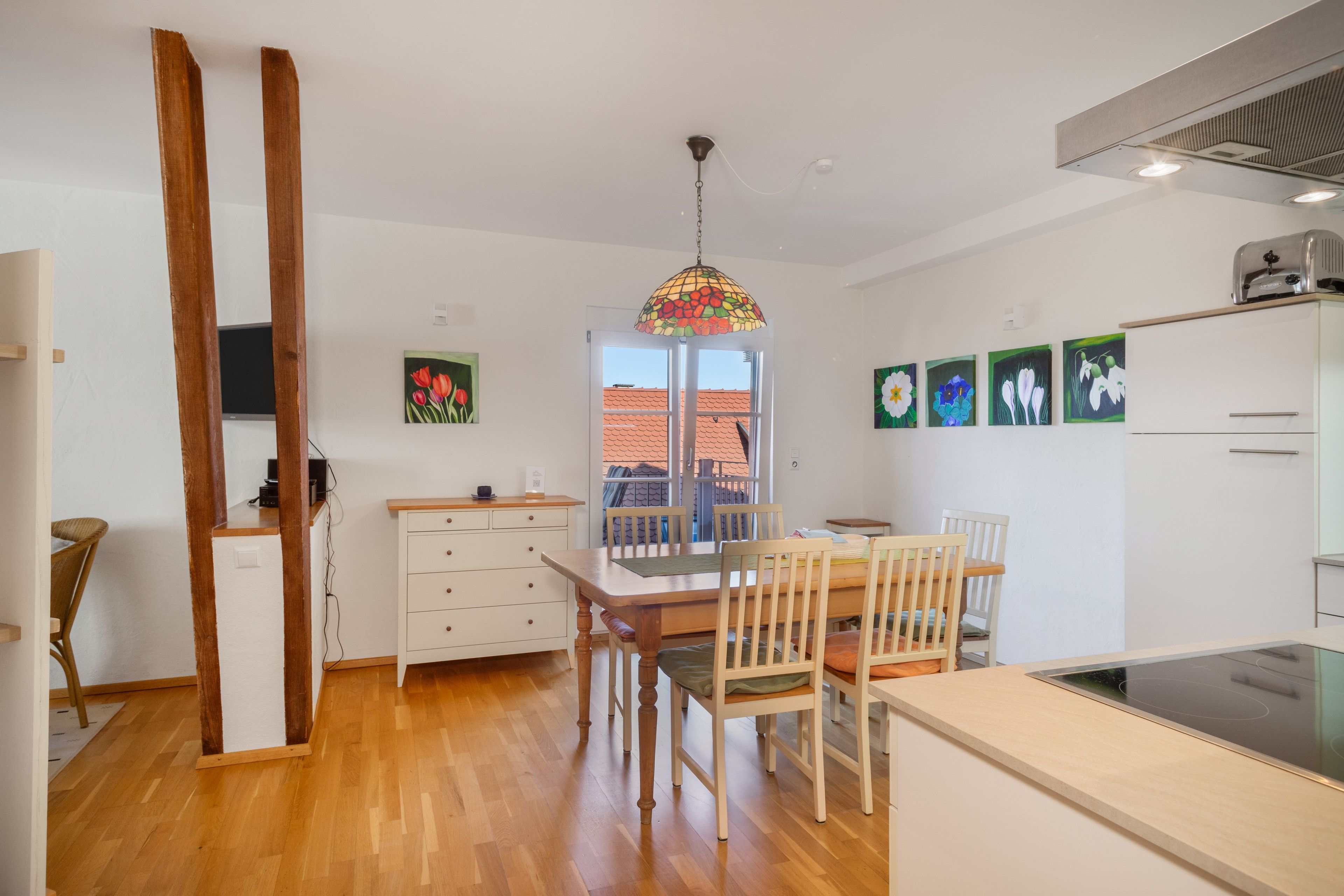 Una cocina moderna con suelo de madera, una mesa de comedor con sillas, un armario blanco y una lámpara colgante.