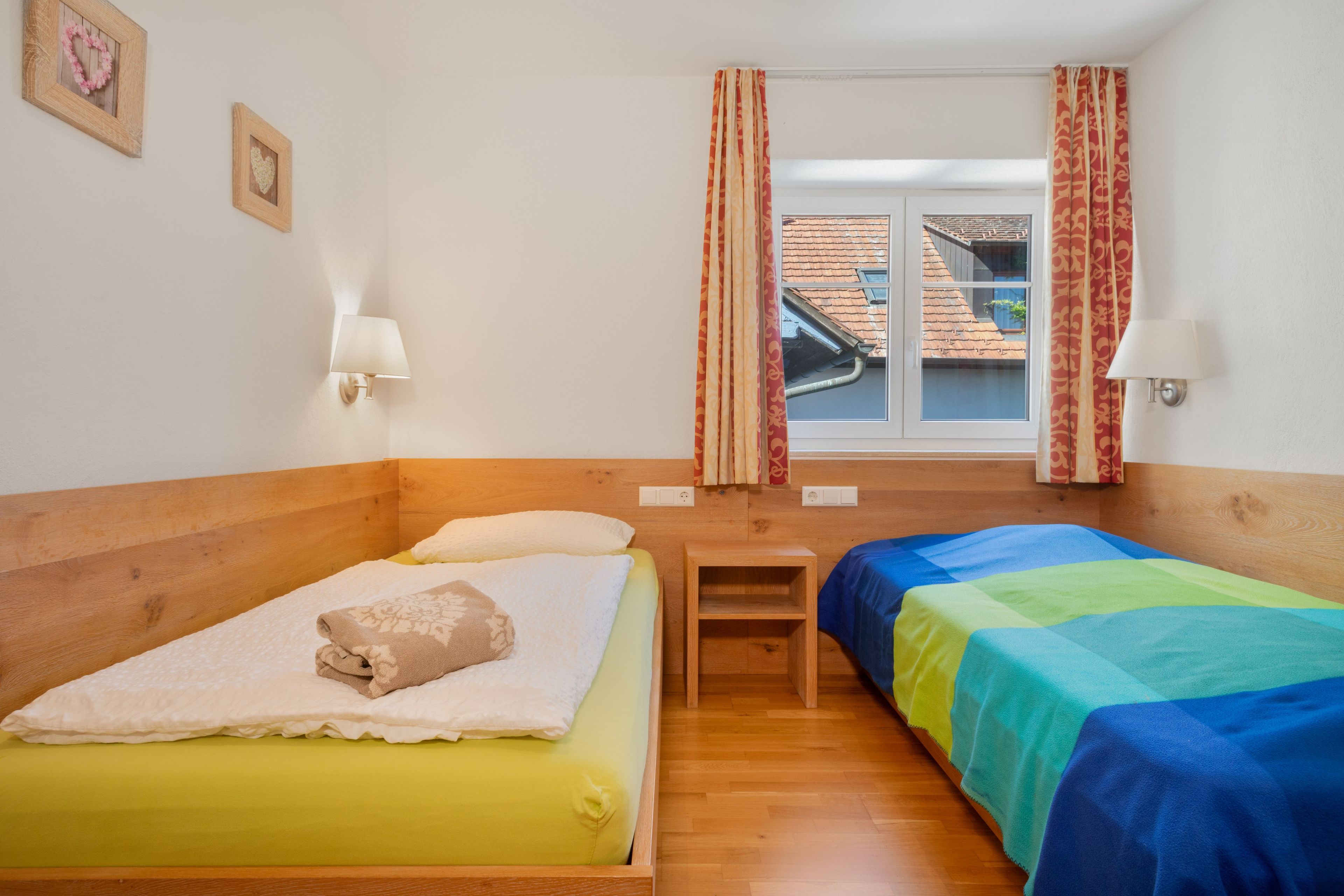 A room with two beds, a wooden headboard, a small table, and a window with curtains.