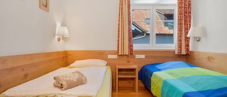 A room with two beds, a wooden headboard, a small table, and a window with curtains.