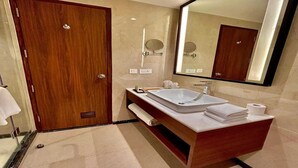 A modern bathroom with a wooden door, a large mirror, a vanity with a sink, and a towel rack. - Superior Checkin Amritsar (Amritsar)