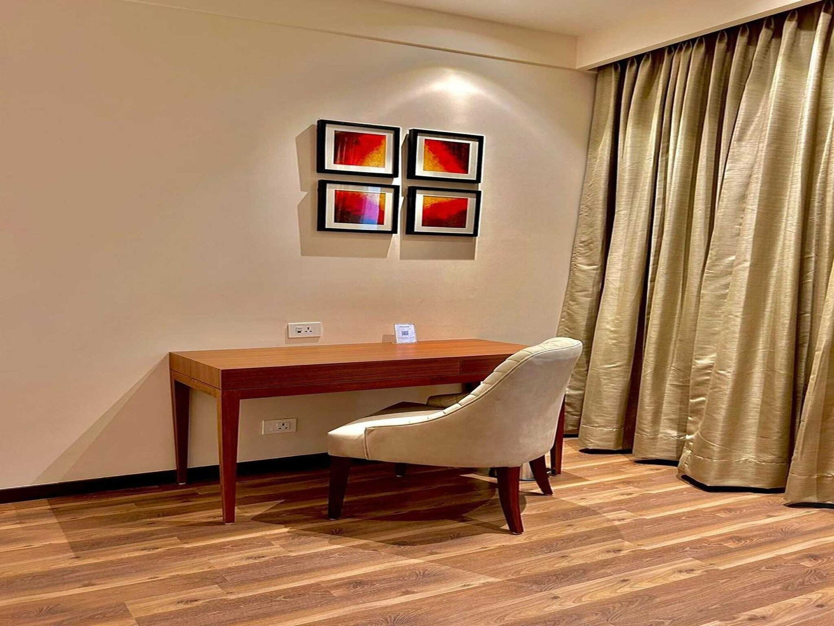 A room with a wooden desk, a white chair, and a wall-mounted artwork.
