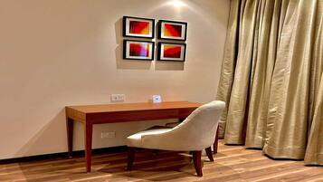 A room with a wooden desk, a white chair, and a wall-mounted artwork.