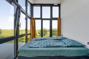 Une chambre avec une grande fenêtre, un lit avec une literie à motifs et des rideaux.