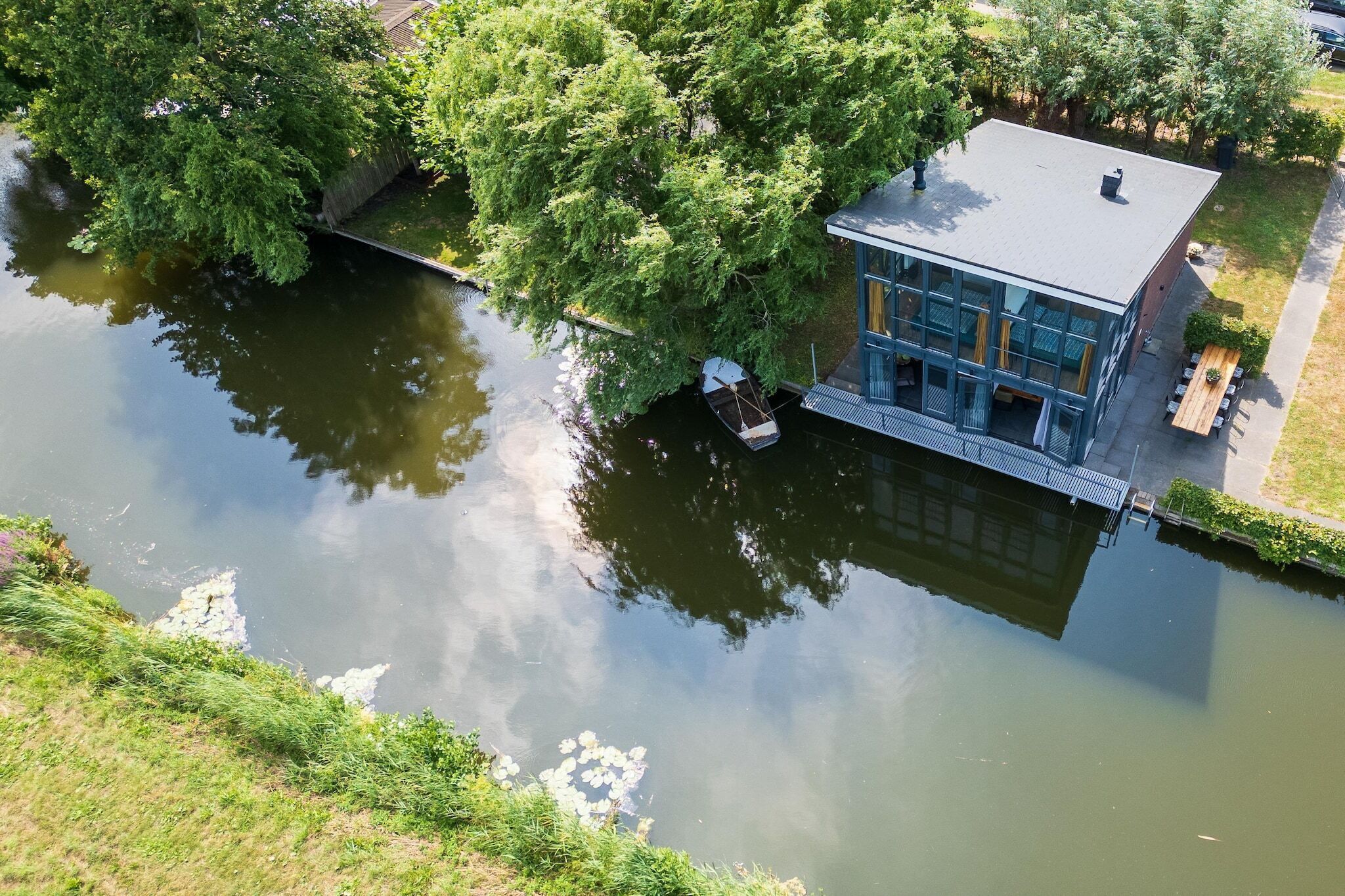 Un edificio junto al río con un muelle, una zona de estar al aire libre techada y vistas al agua.