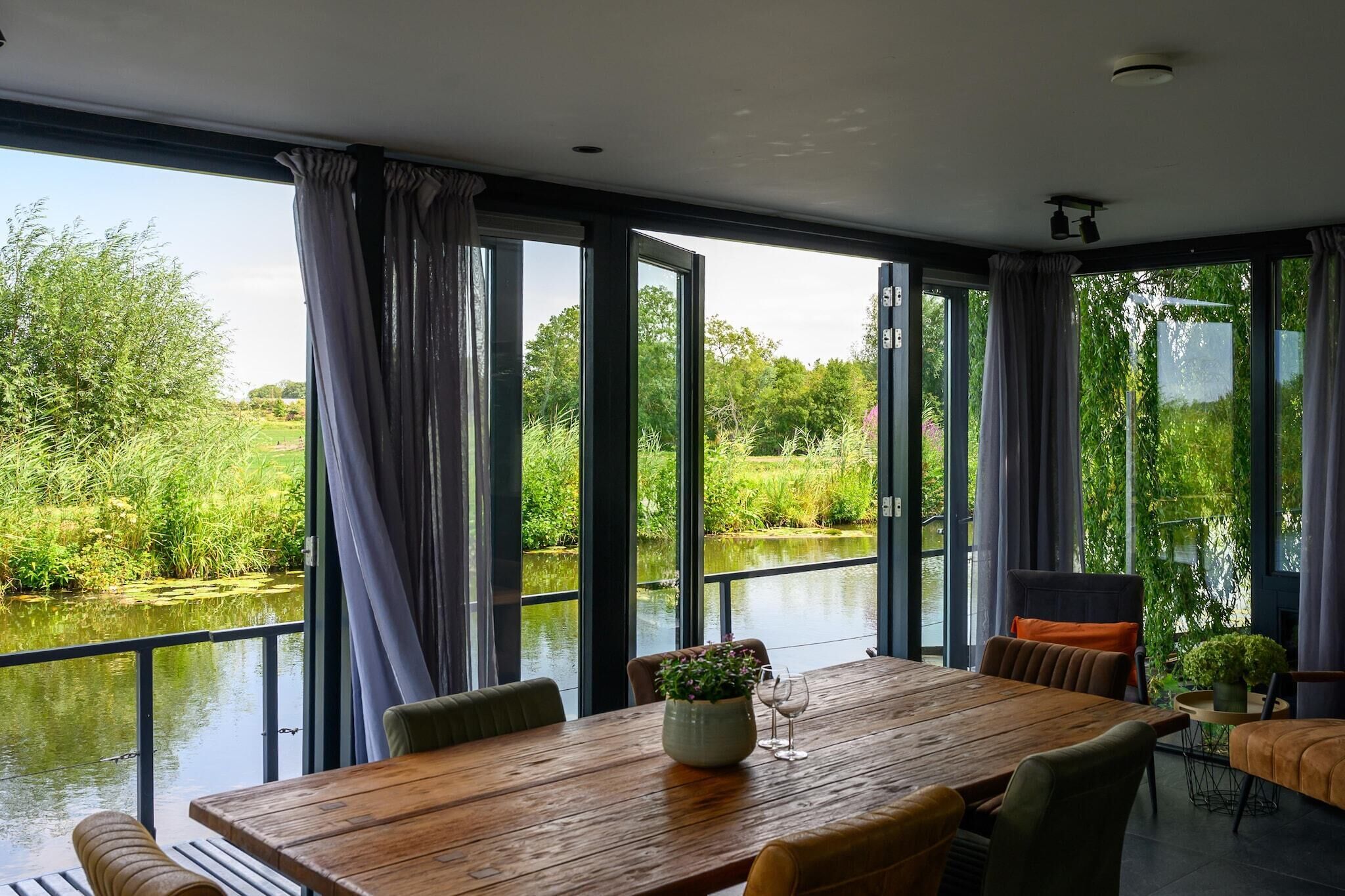 Un espace repas avec une table en bois, des chaises et une vue sur une rivière et la verdure environnante.