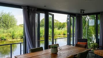 Een eetgedeelte met een houten tafel, stoelen en uitzicht op een rivier en groen.