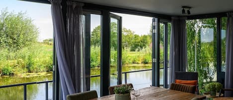 A dining area with a wooden table, chairs, and a view of a river and greenery.