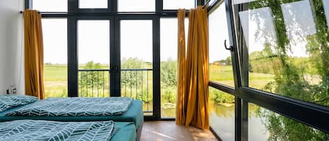 A bedroom with a large window, a bed, and curtains.