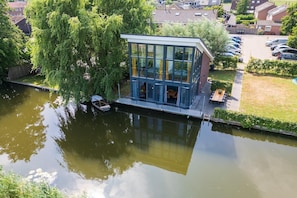 Un edificio moderno con grandes ventanales, un pequeño muelle y un espacio verde con una mesa y sillas.