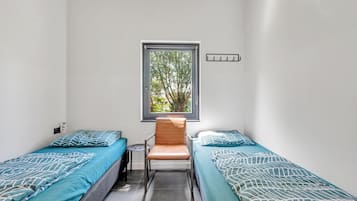 Een kleine kamer met twee eenpersoonsbedden, een stoel, een raam en een lichtschakelaar op de muur.