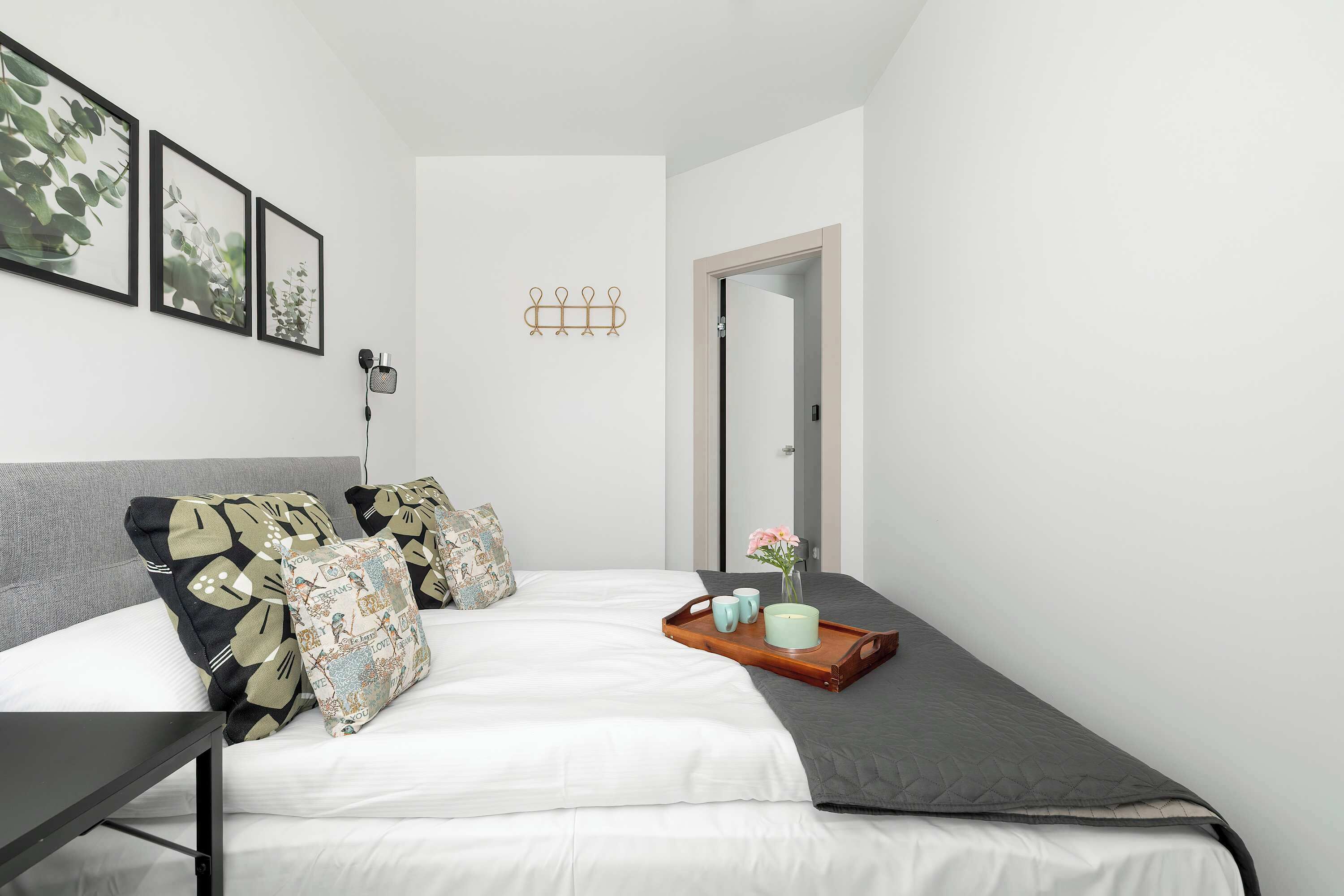 Un dormitorio moderno con cama, almohadas, una mesita de noche, una lámpara de pared y una puerta.