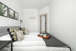 Ein modernes Schlafzimmer mit einem Bett, Kissen, einem Nachttisch, einer Wandlampe und einer Tür.