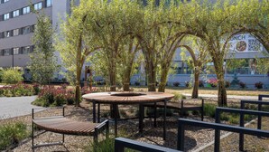 Un espace extérieur aménagé avec une table ronde en bois et des bancs, entouré de plantes de bambou et d’arbustes à fleurs.