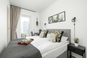 Quarto moderno com cama, mesas de cabeceira, escrivaninha e janela com cortinas.