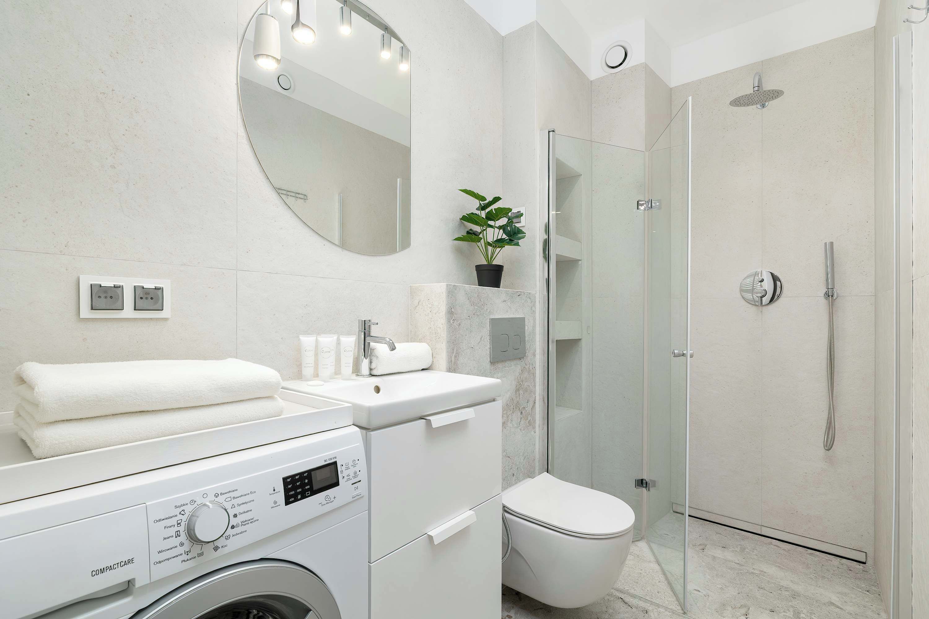 A modern bathroom with a washing machine, a toilet, a sink, and a shower.