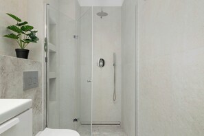 Un bany modern amb dutxa de vidre, una planta en test i un lavabo blanc.