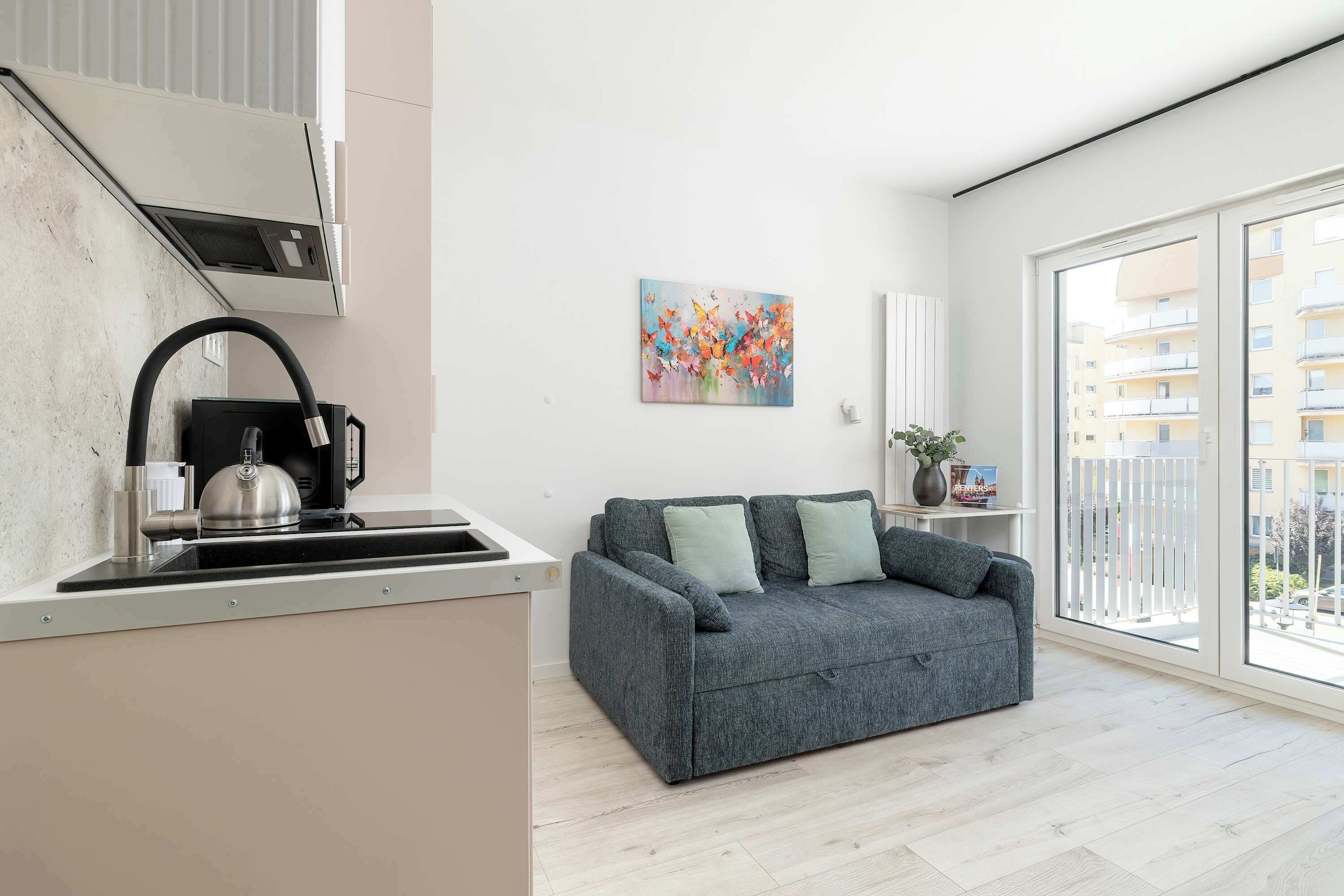 A modern kitchen with a kettle, a sink, and a window overlooking a balcony.