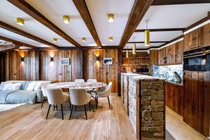 A modern kitchen with wooden walls, a stone island, and a dining area with a round table and chairs.