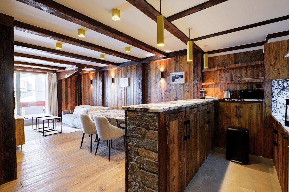 A modern kitchen with wooden accents, a stone island, and a dining area with a sofa and chairs.