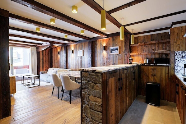 A modern kitchen with wooden accents, a stone island, and a dining area with a sofa and chairs.