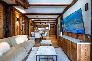 Een modern interieur met een houten wand, een bank, een eethoek en een televisie waarop een racegame wordt vertoond.