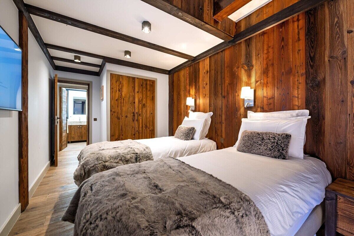 Ein Hotelzimmer mit zwei Betten, Holzvertäfelung und einem Gang zu einem weiteren Zimmer.