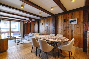 A room with a wooden paneled wall, a round table with chairs, a sofa, and a window with curtains. - Luxury suite 2BR - balcony Courchevel PARK (Courchevel)
