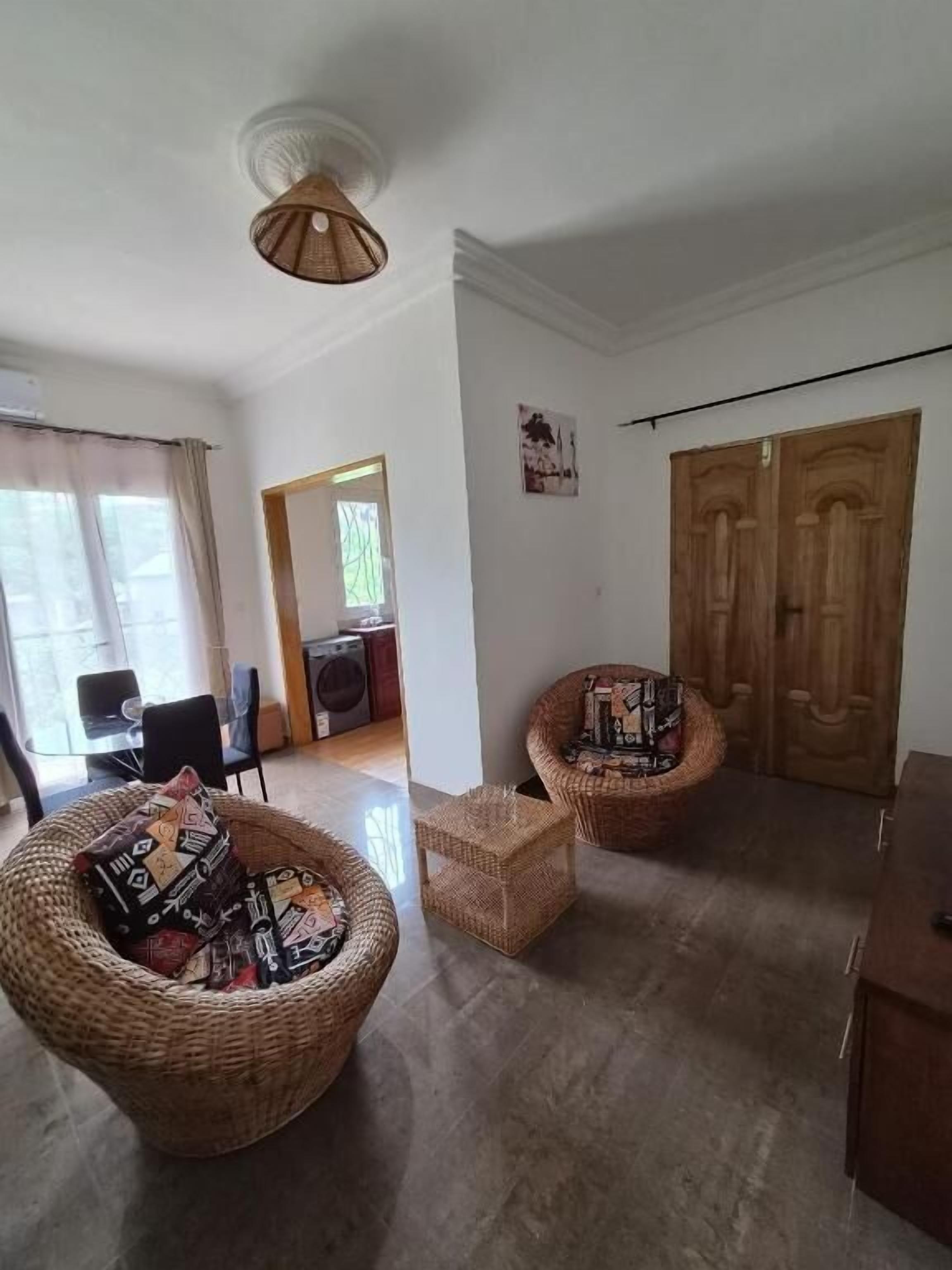 A room with two wicker chairs, a small table, a wooden cabinet, and a ceiling fan.