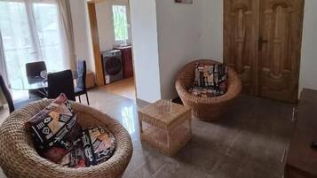 Una habitación con dos sillones de mimbre, una mesita, un armario de madera y un ventilador de techo.