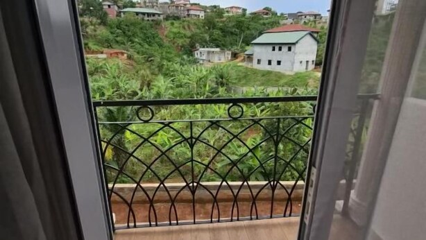 Varanda com piso de madeira e guarda-corpo metálico, com vista para uma área residencial com casas e vegetação.
