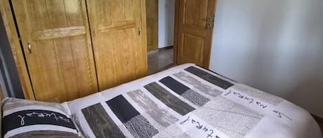 Un dormitorio con un armario de madera, una cama con colcha estampada y techo de madera.