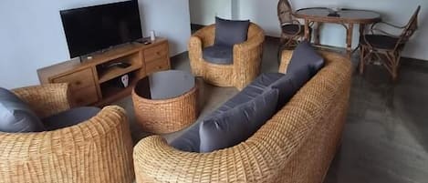 Una sala de estar con muebles de mimbre, un televisor de pantalla plana y un comedor con una mesa redonda y sillas.