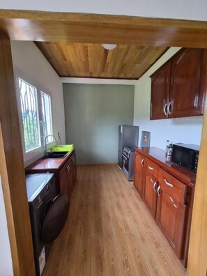 Cozinha compacta com armários de madeira, geladeira e micro-ondas.