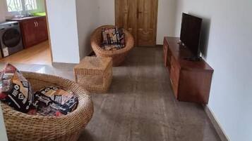 Una sala de estar con un televisor sobre un mueble de madera, un sofá de mimbre y una silla de mimbre.