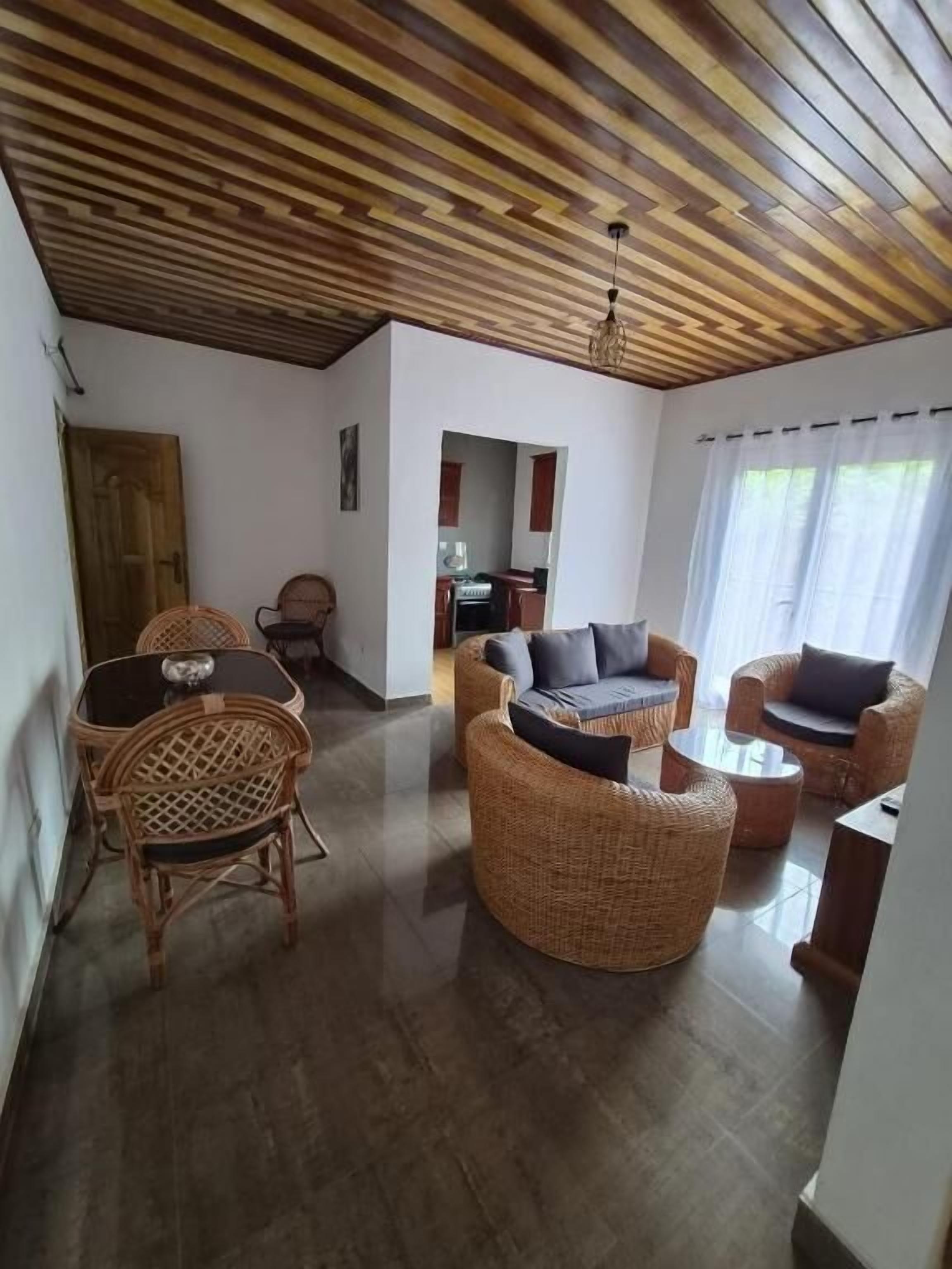 Ein geräumiges Wohnzimmer mit Rattanmöbeln, Holzbalkendecke und Blick zur Küche.