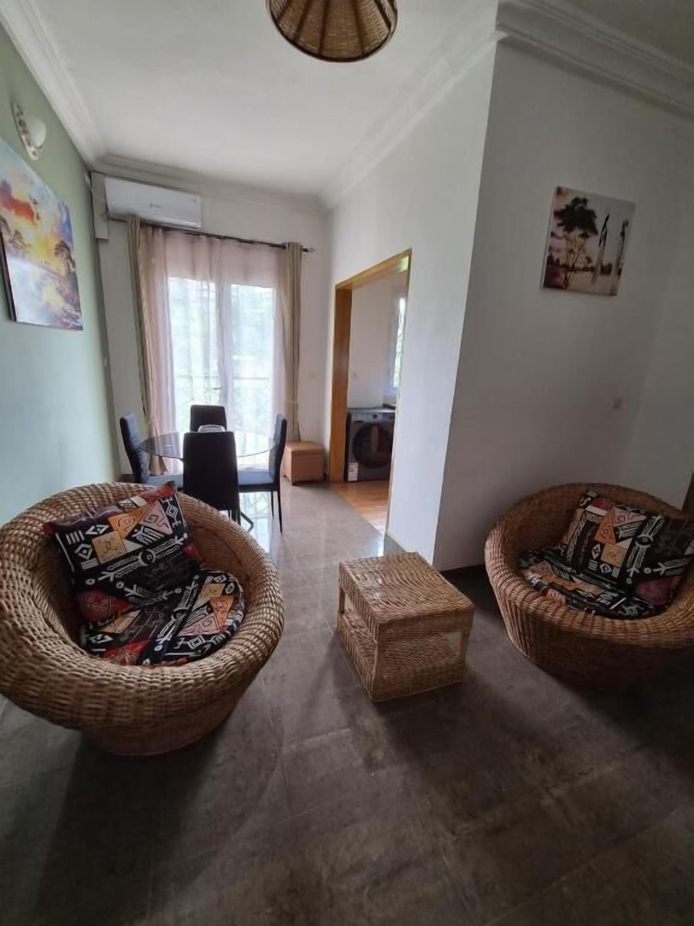 Ein Wohnzimmer mit zwei Korbstühlen, einem kleinen Tisch und einer Tür zu einem anderen Raum.