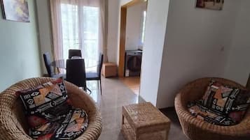 Un salón con dos sillones de mimbre, una mesita y un acceso a otra habitación.