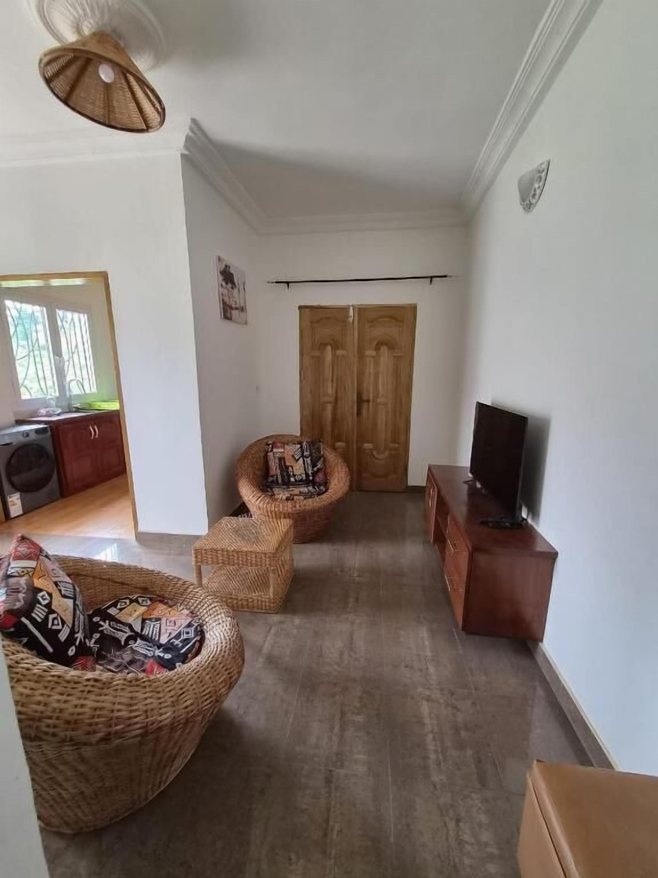 A living room with a television on a wooden cabinet, a wicker sofa, and a wicker chair.