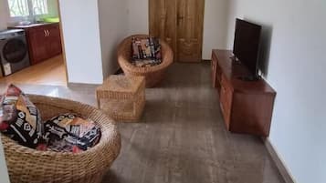 Una sala de estar con un televisor sobre un mueble de madera, un sofá de mimbre y una silla de mimbre.