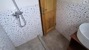A bathroom with a shower, a wooden door, a sink, and a tiled floor. - Charming 2-bedroom Apartment in Yaoundé - Comfortable Living (Yaoundé)