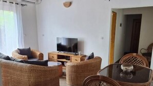 A living room with wicker furniture, a glass table, and a television. - Charming 2-bedroom Apartment in Yaoundé - Comfortable Living (Yaoundé)