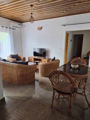A living room with wicker furniture, a glass table, and a television. - Charming 2-bedroom Apartment in Yaoundé - Comfortable Living (Yaoundé)
